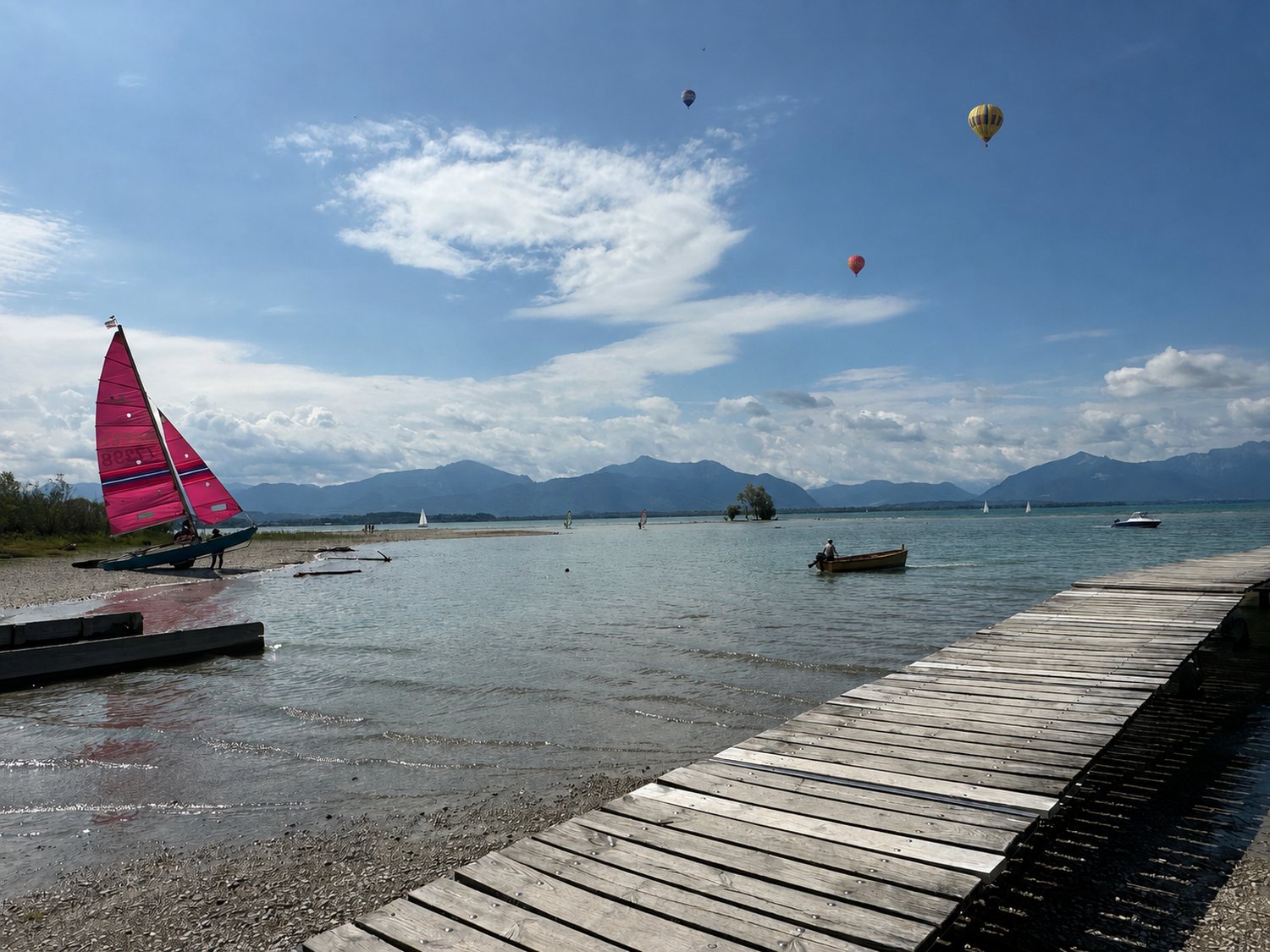 Chiemsee-Panorama mit Segelbooten, Fischern, Surfern und Ballonen vor den Alpen